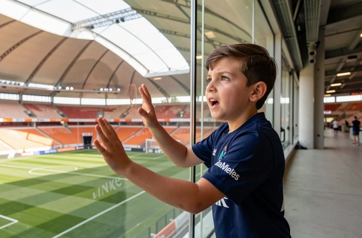 Jeune garçon en maillot de l'OM admirant la pelouse depuis les coulisses de l'Orange Vélodrome à Marseille